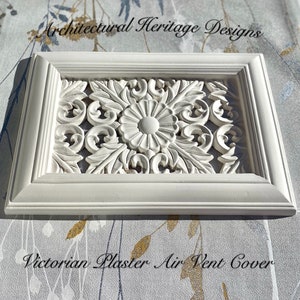 May include: White plaster air vent cover with a decorative floral design. The cover is framed with a simple white moulding. "Architectural Heritage Designs" and "Victorian Plaster Air Vent Cover" are printed on the background.