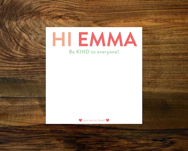 May include: White card with the text "HI EMMA" in pink and red letters. The text "Be KIND to everyone!" is written in green below the name. The bottom of the card has two red hearts and the text "you are so loved".