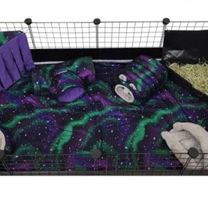 May include: A rectangular black wire pet cage containing a soft fabric liner with a purple and green aurora borealis pattern. Inside are two beige plush beds, a purple fabric corner hideout with fringe, a matching tunnel, and a black hay rack.
