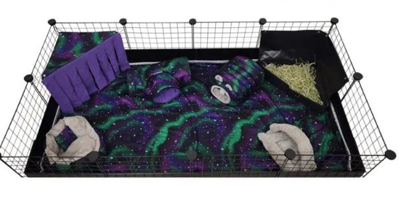 May include: A rectangular black wire pet cage containing a soft fabric liner with a purple and green aurora borealis pattern. Inside are two beige plush beds, a purple fabric corner hideout with fringe, a matching tunnel, and a black hay rack.