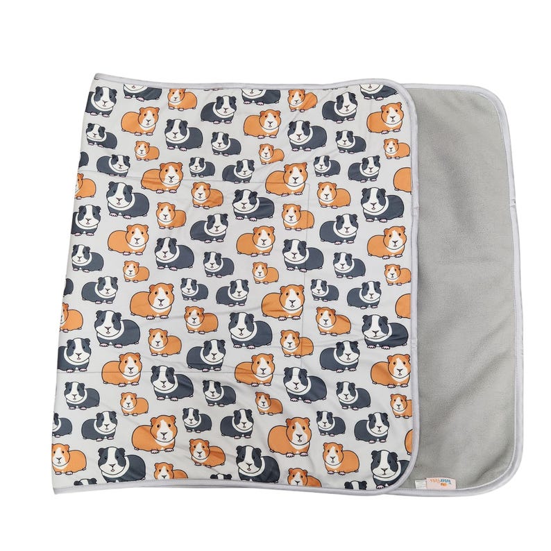 May include: A rectangular blanket featuring a repeating pattern of cartoon guinea pigs in shades of orange, black, and white on a light gray background. The blanket has a solid light gray underside and is finished with a light gray fabric trim.
