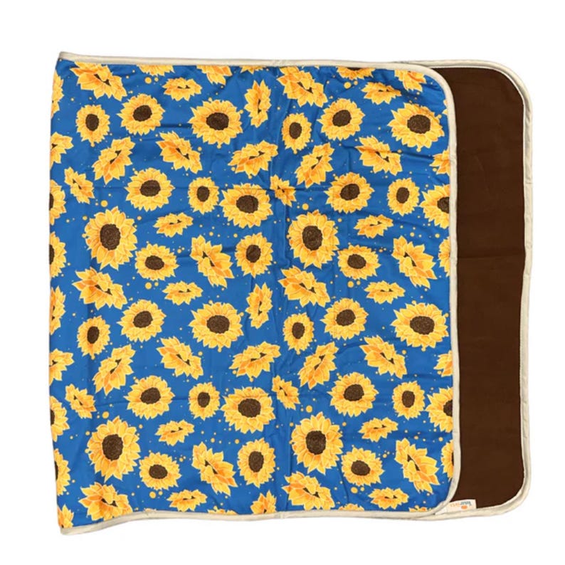 K&ouml;nnte beinhalten: Eine rechteckige Decke mit einem leuchtend blauen Hintergrund und einem sich wiederholenden Muster aus gelben Sonnenblumen mit dunkelbraunen Mitten. Die Decke hat eine einfarbige dunkelbraune Unterseite und ist mit einem hellen cremefarbenen Rand versehen.