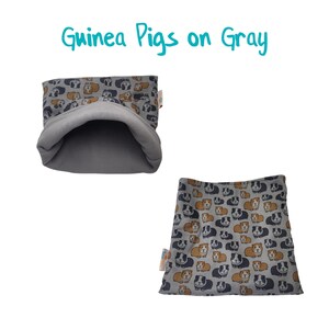 May include: A gray fleece guinea pig bed with a pattern of brown and black guinea pigs. The bed is shaped like a tunnel and has a flat bottom.