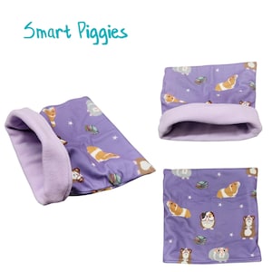 May include: Purple fleece-lined guinea pig sleeping bag with a print of guinea pigs wearing glasses and reading books. The text "Smart Piggies" is written above the sleeping bag.