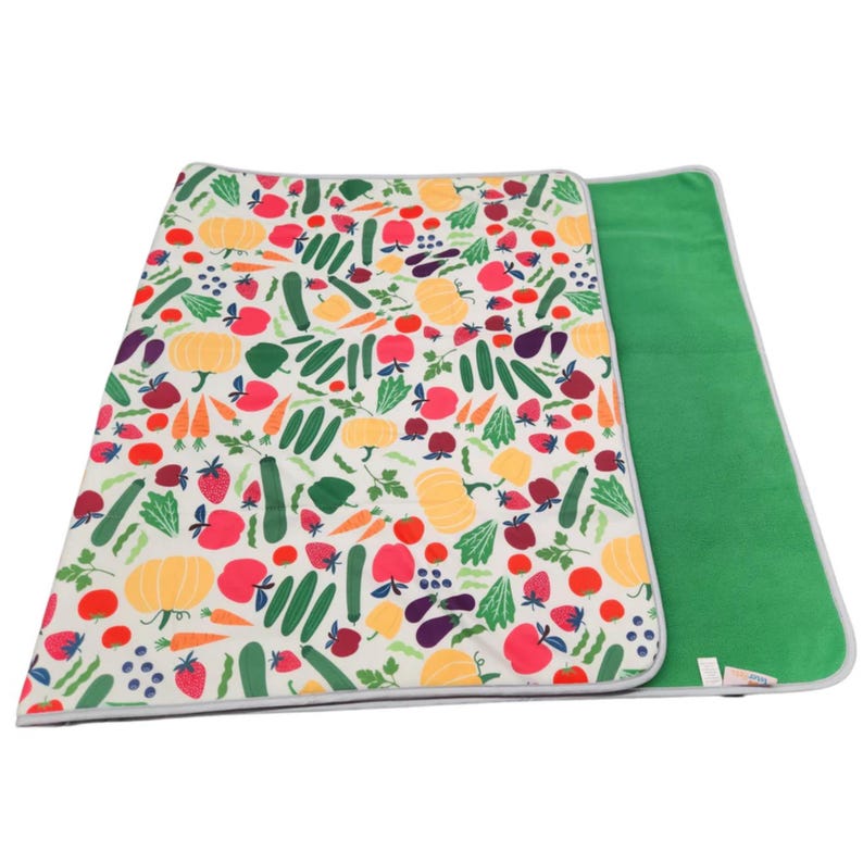 May include: A rectangular mat featuring a white background with a colorful pattern of various fruits and vegetables including yellow pumpkins, red apples, green cucumbers, carrots, and strawberries. The reverse side is a solid bright green fabric.