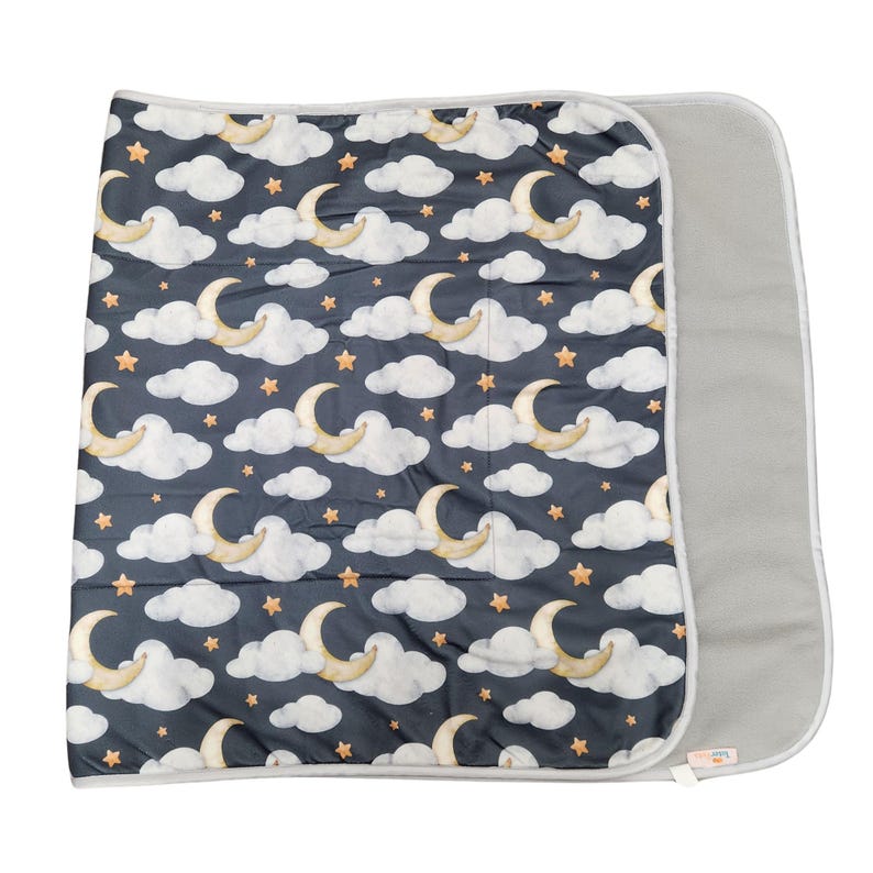 May include: A rectangular blanket featuring a dark navy blue background with a repeating pattern of watercolor-style white clouds, golden crescent moons, and small orange stars. The blanket has a solid light gray underside and gray trim.