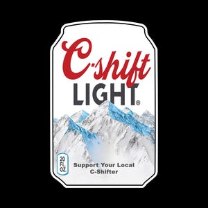 May include: A white sticker in the shape of a can, featuring the text "C-shift LIGHT" in red and black. Below the text is a mountain range with snow-capped peaks. The sticker also includes the text "Support Your Local C-Shifter" and "20 FL OZ."