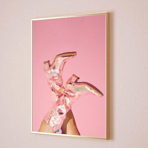 May include: A pair of pink cowboy boots with a metallic finish are propped up against a pink background. The boots are in focus and the background is blurred.