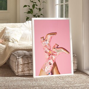 May include: A framed print of a pair of pink cowboy boots with a floral pattern on a pink background.