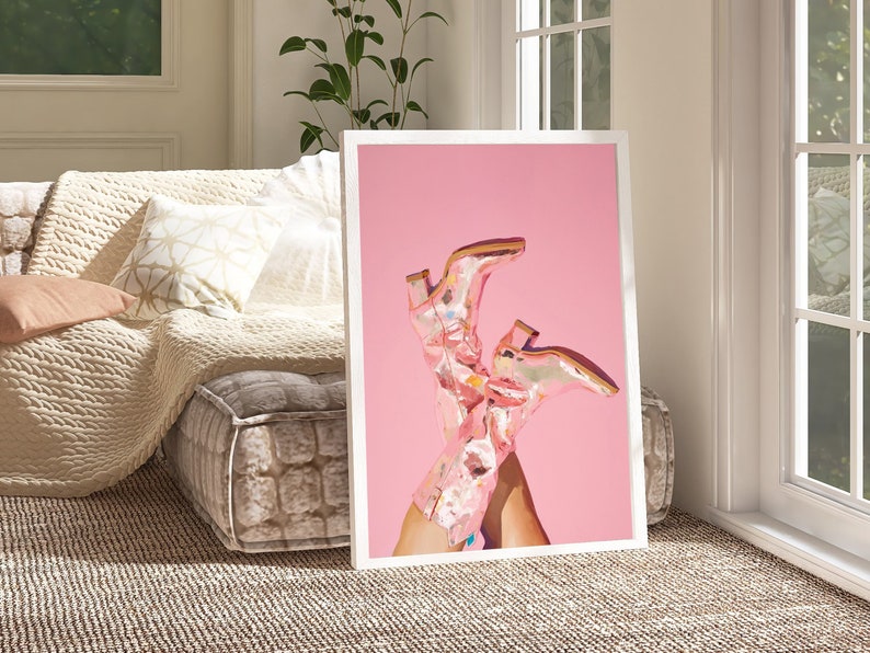 May include: A framed print of a pair of pink cowboy boots with a floral pattern on a pink background.