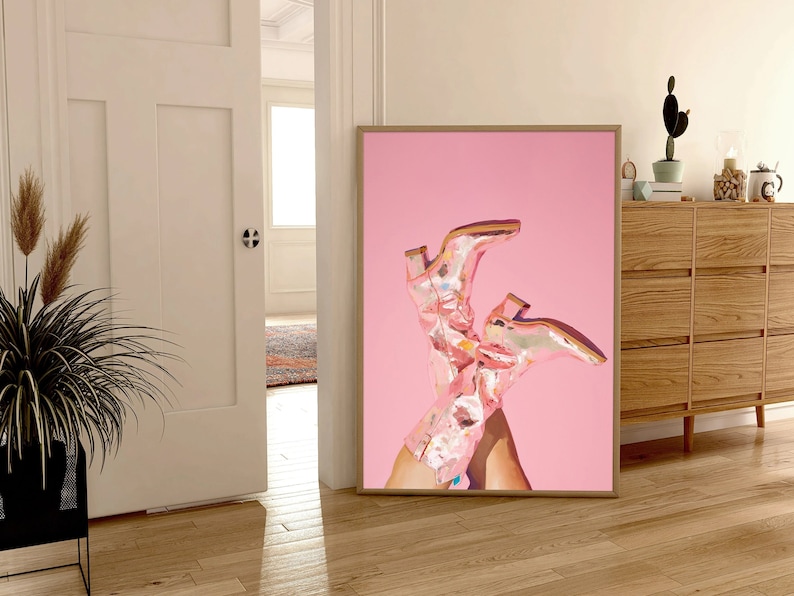 May include: A framed print of a pair of pink cowboy boots with floral patterns on a pink background.