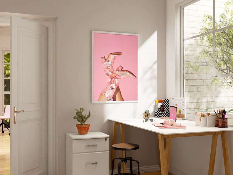 May include: A framed print of a pair of pink cowboy boots on a pink background.