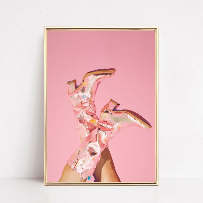 May include: A pair of pink cowboy boots with a metallic finish and floral pattern are propped up against a pink background.