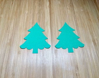 May include: Two teal green paper Christmas tree cutouts on a wood background.