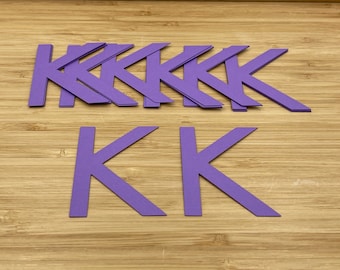 Puede incluir: Un conjunto de letras de papel morado que deletrean la letra "K" varias veces. Las letras están apiladas unas sobre otras.
