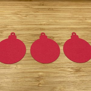 Könnte beinhalten: Drei rote Weihnachtsbaumschmuck-Ausschnitte aus Papier auf einer Holzoberfläche.