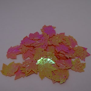 Könnte beinhalten: Ein Haufen regenbogenfarbener, pinkfarbener und gelber, blattförmiger Pailletten. Die Pailletten sind aus Kunststoff und haben eine glänzende Oberfläche.