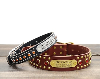 May include: Two leather dog collars. One is black with orange gems and the name "Sandy" on a silver plate. The other is brown with red gems and the name "Scooby" on a gold plate. Both collars have metal studs.