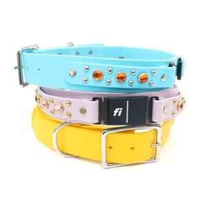 May include: A stack of three dog collars in pastel colors. The top collar is light blue with orange jewels. The middle collar is lavender with pink jewels. The bottom collar is yellow with a silver buckle. Each collar has a silver buckle.