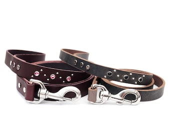 May include: Two leather dog leashes with silver clasps. One leash is brown with pink rhinestones and the other is black with silver studs.