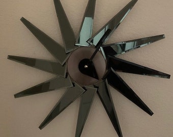 May include: A black and silver clock with a unique design. The clock face is hidden behind a series of mirrored, pointed blades that form a starburst pattern.