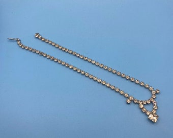 May include: A silver rhinestone necklace with a teardrop-shaped pendant. The necklace is made of small, clear rhinestones that are set in a silver metal.
