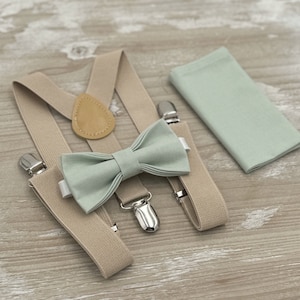 Puede incluir: Un conjunto de pajarita, tirantes y pañuelo de bolsillo de color verde claro. Los tirantes son de color beige con un detalle de cuero marrón. La pajarita y el pañuelo de bolsillo están hechos de una tela suave de color verde claro.