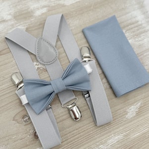May include: A set of gray suspenders with a light blue bow tie and a matching pocket square. The suspenders have silver clips and the bow tie is made of a soft fabric.