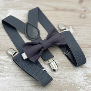 May include: A dark gray bow tie and suspenders set. The bow tie is made of a soft fabric and has a classic shape. The suspenders are adjustable and have silver clips.