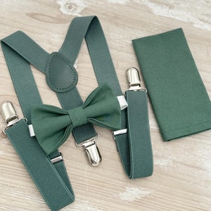May include: A green bow tie, suspenders, and pocket square set. The bow tie and suspenders are made of a textured fabric and have silver clips. The pocket square is a solid green.