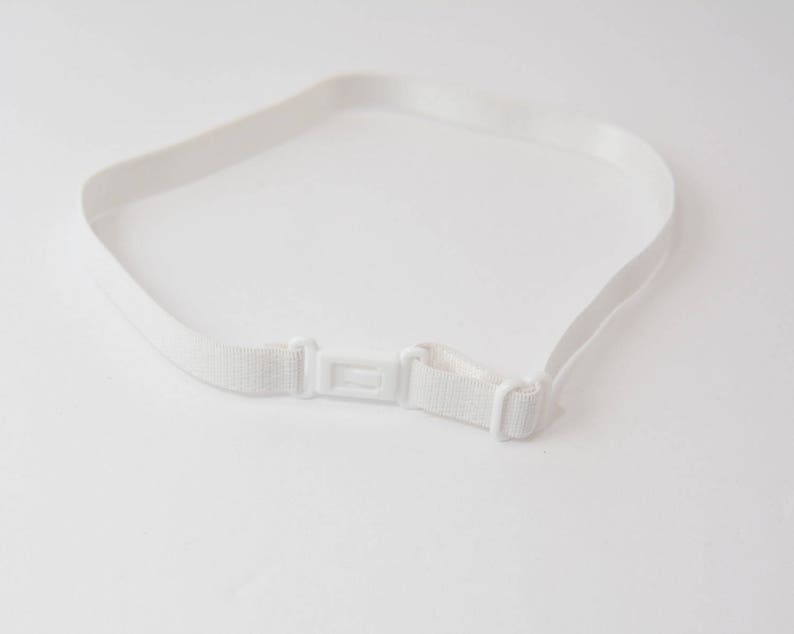 Może przedstawiać: Biały elastyczny pasek z plastikową klamrą. Pasek jest przeznaczony do utrzymywania odzieży w miejscu.