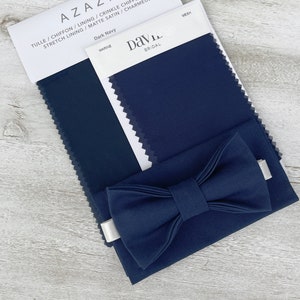 Może przedstawiać: Pr&oacute;bka tkaniny w kolorze ciemnoniebieskim z nadrukiem "Dark Navy" i "Marine". Na pr&oacute;bce leży muszka wykonana z tej samej tkaniny. Na białej etykiecie widnieje napis "Davie Bridal".