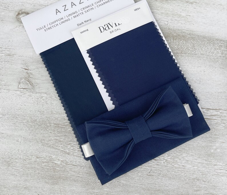 Może przedstawiać: Pr&oacute;bka tkaniny w kolorze ciemnoniebieskim z nadrukiem "Dark Navy" i "Marine". Na pr&oacute;bce leży muszka wykonana z tej samej tkaniny. Na białej etykiecie widnieje napis "Davie Bridal".