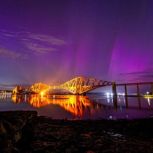 Könnte beinhalten: Blick auf eine Brücke, die nachts beleuchtet ist, mit einer violetten Aurora Borealis am Himmel.