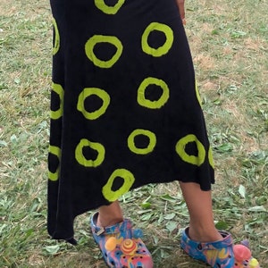 May include: A black maxi skirt with a green circle pattern. The skirt is asymmetrical and has a flowy silhouette. The person is wearing colorful clogs with embellishments.