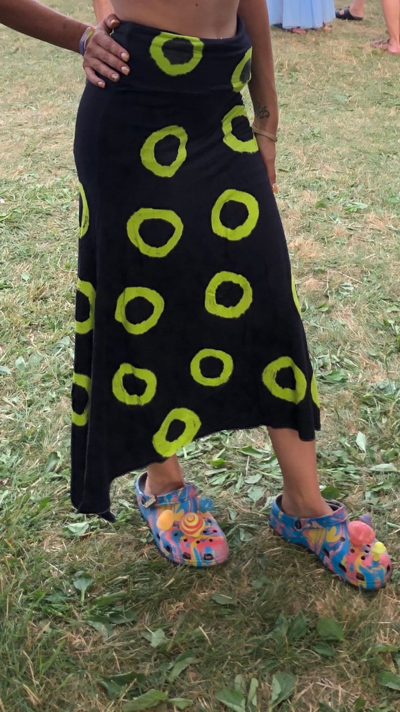 May include: A black maxi skirt with a green circle pattern. The skirt is asymmetrical and has a flowy silhouette. The person is wearing colorful clogs with embellishments.