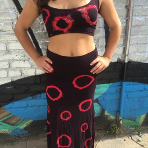 May include: A black crop top with red tie-dye circles and a matching black skirt with red tie-dye circles. The skirt is a maxi skirt that falls to the ankles.