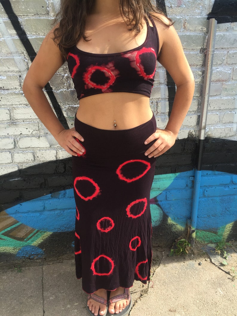 May include: A black crop top with red tie-dye circles and a matching black skirt with red tie-dye circles. The skirt is a maxi skirt that falls to the ankles.