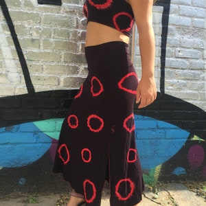 May include: A black skirt and matching crop top with a red circle tie-dye pattern. The skirt has a slit on the side.