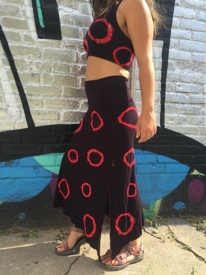 May include: A black skirt and matching crop top with a red circle tie-dye pattern. The skirt has a slit on the side.