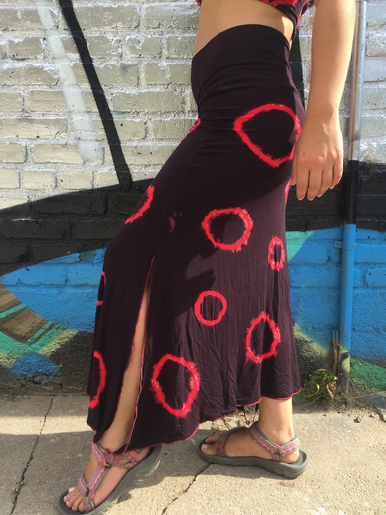 May include: A long black skirt with a side slit and a red circle pattern. The skirt is made of a soft, flowing fabric.