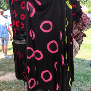 May include: A black skirt with pink and white tie-dye circles. The skirt has a slit on the side and is hanging on a rack.