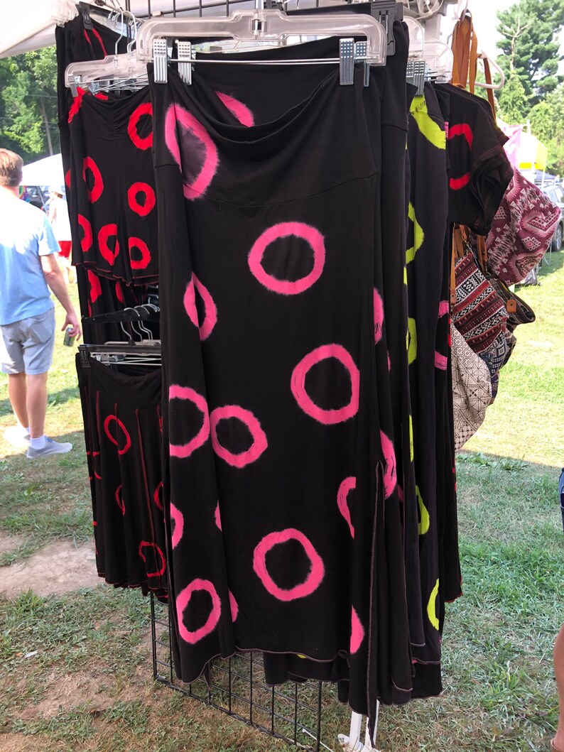 May include: A black skirt with pink and white tie-dye circles. The skirt has a slit on the side and is hanging on a rack.