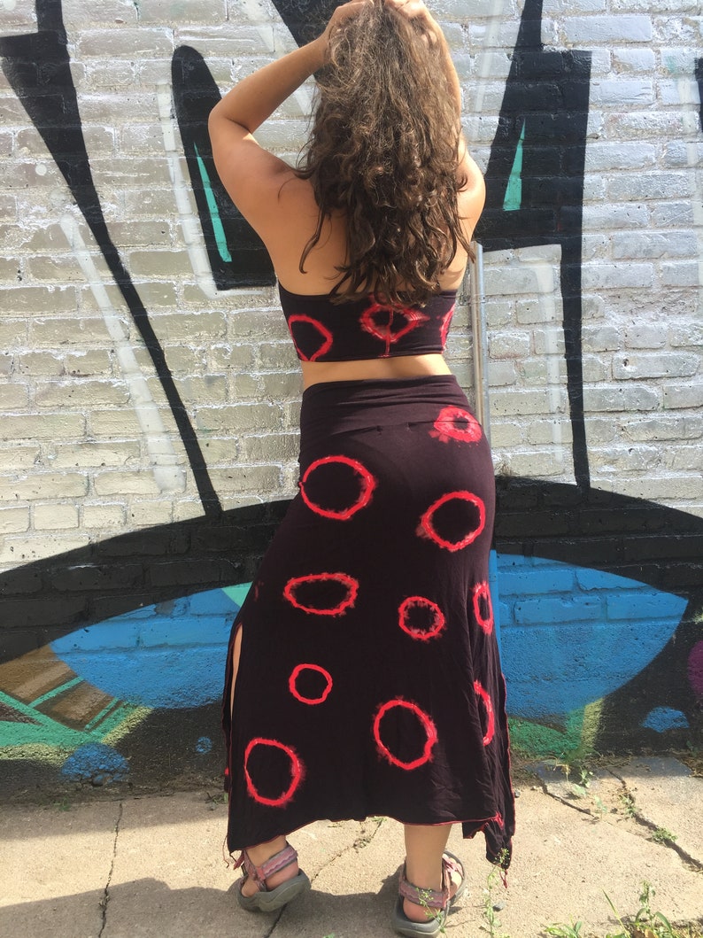 May include: A black skirt with a red tie-dye pattern and a side slit. The skirt is long and flowy, and it has a high waist.