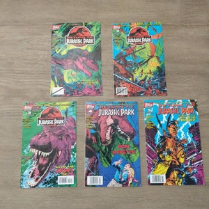 May include: Five comic books featuring the Jurassic Park franchise. The covers feature colorful illustrations of dinosaurs, characters, and action scenes. The titles include "Jurassic Park", "Return to Jurassic Park", and "Jurassic Park: Raptor and the Thunder".