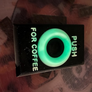 May include: A black plastic button with a green ring in the center. The button says "PUSH" and "FOR COFFEE" in white text.