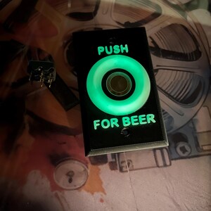 May include: A black plastic button with a green illuminated circle that reads "PUSH FOR BEER".