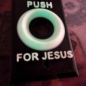 May include: A black plastic button with a white ring around it. The button says "PUSH FOR JESUS" in white letters.