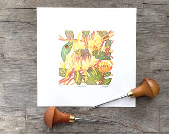 May include: A square art print with a botanical illustration of yellow and orange flowers, green leaves, and a red ladybird. Two wood-handled carving tools are on a wooden surface.