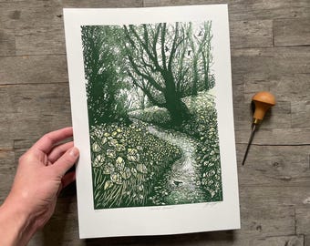 May include: A green and white linocut print of a woodland stream with a single tree in the background. The print is titled "Woodland Stream" and signed by the artist.